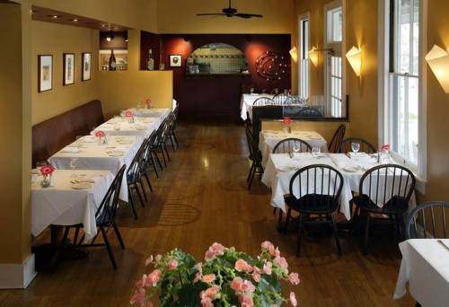 A cozy restaurant interior with white tablecloths, black chairs, and flower centerpieces, featuring warm yellow walls.