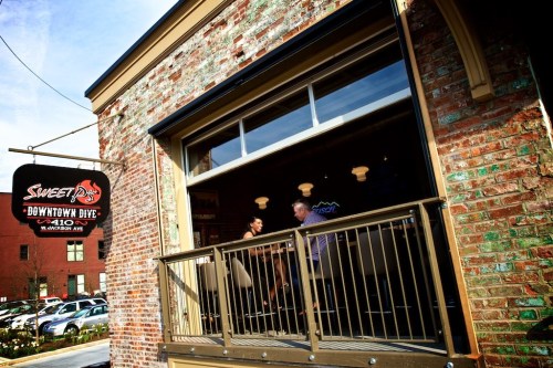 A brick building with a sign for "Sweet D's Downtown Dive" and people visible through the large windows.