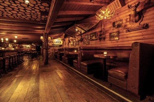 Cozy rustic interior of a bar with wooden walls, booths, and dim lighting, featuring Sasquatch-themed decor.