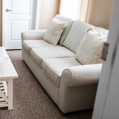 A cozy living room with a light-colored sofa and decorative pillows, featuring a small coffee table and beige carpet.