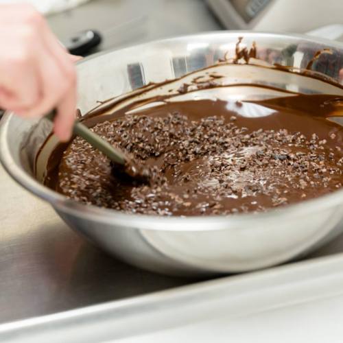 A hand stirs a bowl of melted chocolate mixed with small chocolate chips.