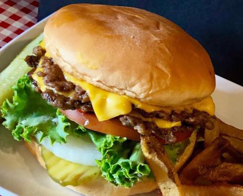 A juicy cheeseburger with lettuce, tomato, pickles, and crispy fries on the side, served on a white plate.