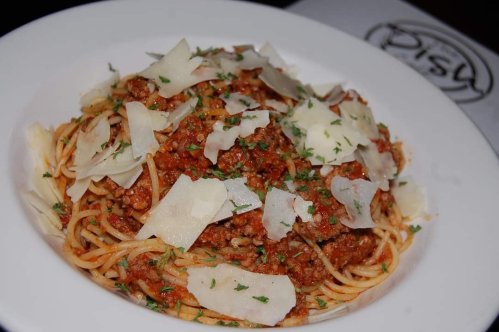 A plate of spaghetti topped with meat sauce, grated cheese, and parsley, served in a white bowl.