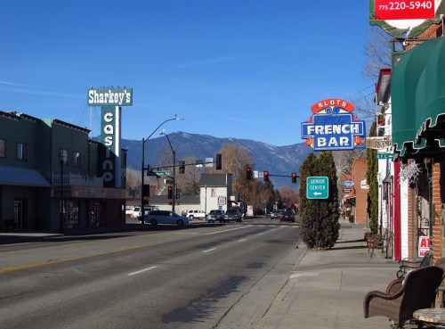 A quiet street scene featuring Sharkey's Casino and French Bar, with mountains in the background and clear blue skies.
