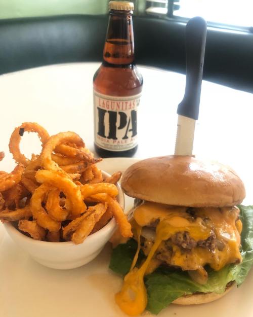 A juicy cheeseburger with melted cheese and lettuce, served with curly fries and a bottle of Lagunitas IPA.