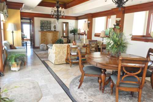 A spacious, elegantly decorated living area with a dining table, plants, and natural light from large windows.