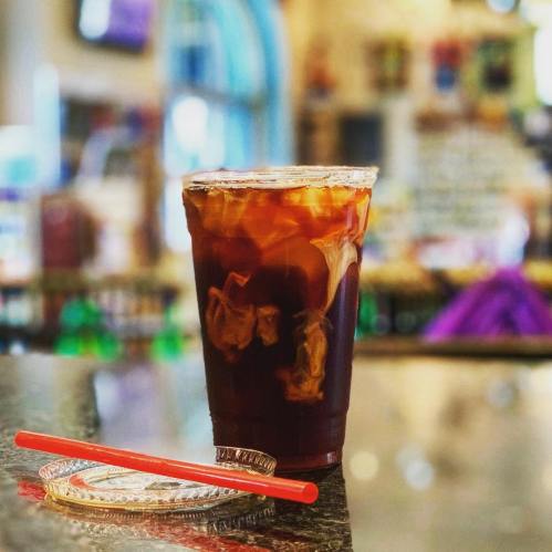 A glass of iced coffee with cream swirling, placed on a countertop with a red straw beside it.