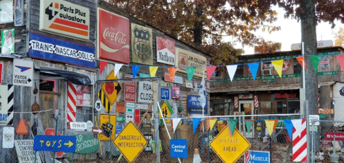 A colorful collection of vintage signs and banners on a rustic building, surrounded by a fence and trees.