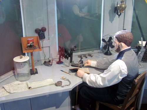 A vintage scene featuring a mannequin at a desk with old tools, a typewriter, and various historical objects.
