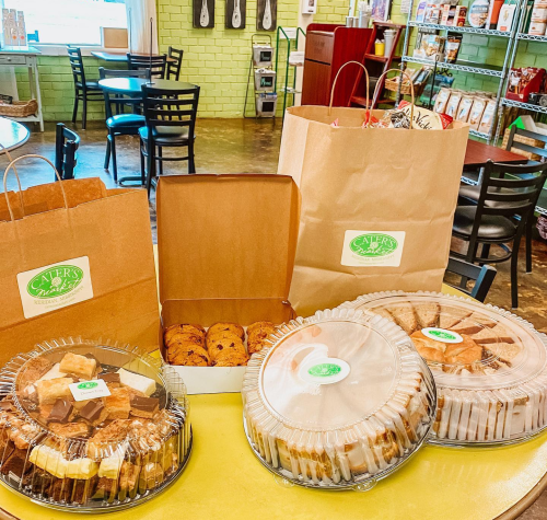 A display of assorted baked goods in containers and bags from a bakery, set on a table in a cozy café.