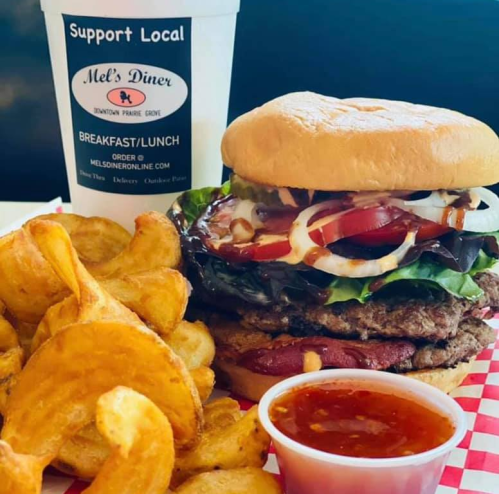 A delicious burger with lettuce, tomato, and onion, served with crispy potato chips and a cup of dipping sauce.