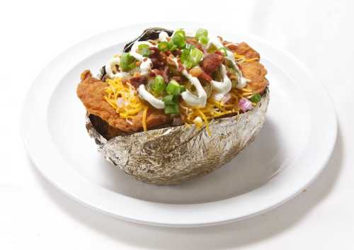 A crispy chicken breast topped with cheese, green onions, bacon, and sour cream, served in a foil-lined bowl.