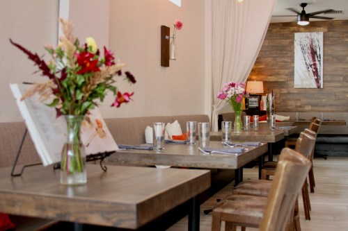 A cozy restaurant interior with wooden tables, chairs, and colorful flower arrangements on the tables.
