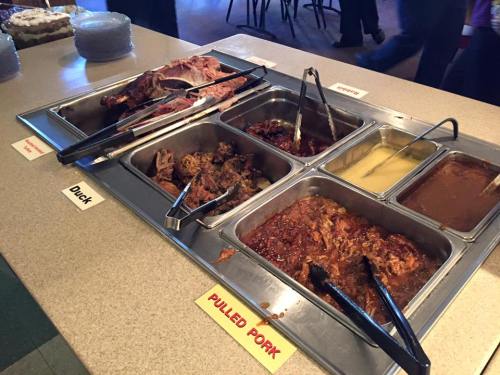 A buffet table with trays of pulled pork, duck, and various sauces, with tongs for serving.