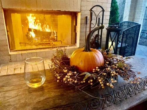 A cozy scene with a pumpkin centerpiece on a wooden table, a glass of drink, and a warm fire in the background.