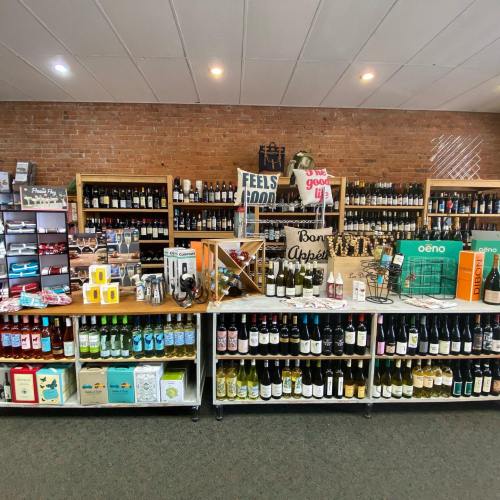 A well-organized wine shop display featuring various bottles, accessories, and promotional signs on wooden shelves.