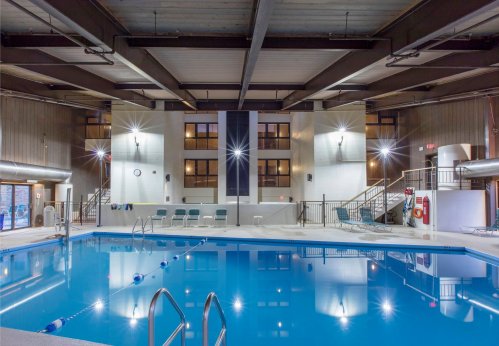 Indoor swimming pool with clear blue water, lounge chairs, and large windows in a modern facility.