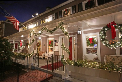 A festive inn decorated with wreaths and lights, featuring a porch and an American flag, set in a cozy evening atmosphere.