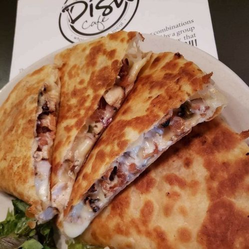 Three crispy quesadillas filled with chicken and cheese, served on a plate with a side of fresh greens.