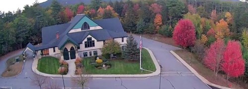 Aerial view of a building surrounded by vibrant autumn trees in shades of red, orange, and green.