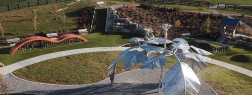 Aerial view of a park featuring a large metal sculpture, landscaped gardens, and colorful play structures.