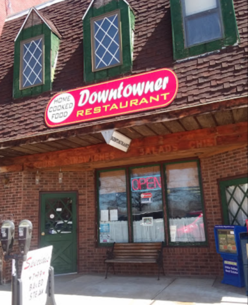 Exterior of the Downtowner Restaurant, featuring a red sign, open window, and a bench outside.
