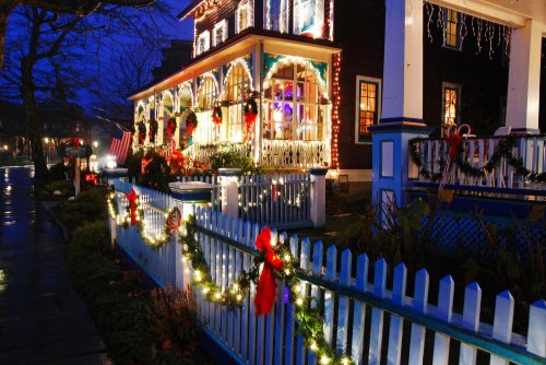 A beautifully decorated house with Christmas lights and wreaths, surrounded by a white picket fence and festive greenery.