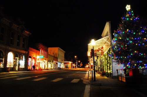 A festive street at night, adorned with colorful Christmas lights and a decorated tree, creating a warm holiday atmosphere.