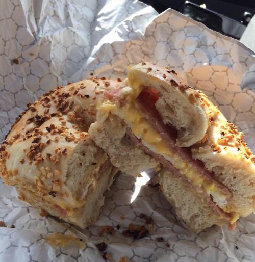 A toasted bagel sandwich filled with ham, cheese, and egg, resting on crumpled paper.