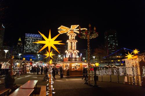 A festive night market with twinkling lights, a carousel, and holiday decorations against a city skyline.