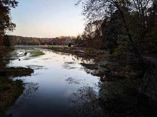 A serene river scene at dusk, surrounded by trees and reflecting the soft colors of the sky.
