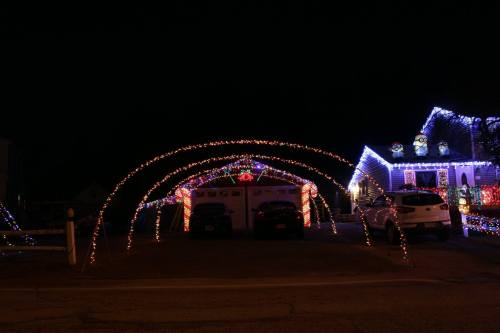 A house decorated with colorful Christmas lights, featuring an arch of lights over the garage and festive displays.