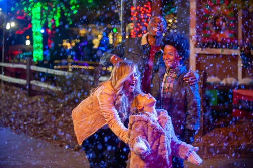 A joyful family enjoys a snowy evening, surrounded by colorful holiday lights, with laughter and smiles all around.