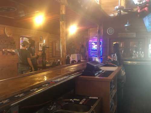 A rustic bar interior with wooden decor, dim lighting, and a bartender preparing drinks in the background.