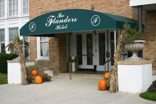 Entrance of The Flanders Hotel, featuring a green awning, pumpkins, and decorative corn stalks.