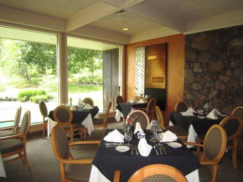 Elegant restaurant interior with tables set for dining, featuring white tablecloths and a view of greenery outside.