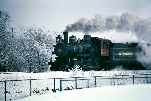 A vintage steam locomotive billows smoke while traveling through a snowy landscape.