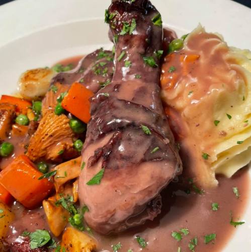 A plate featuring a glazed chicken drumstick, mashed potatoes, and mixed vegetables in a rich sauce, garnished with herbs.