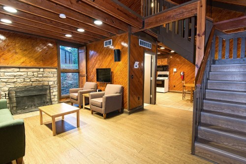 Cozy wooden interior of a cabin with a fireplace, seating area, and stairs leading to an upper level.