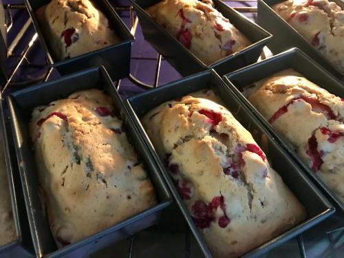 Freshly baked loaves of bread with red fruit, cooling in metal pans inside an oven.