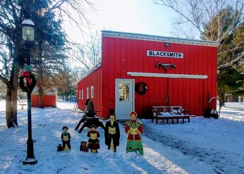 A red building labeled "Blacksmith" surrounded by snow, with festive decorations and wooden figures in front.