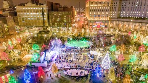 Aerial view of a festive park at night, adorned with colorful lights and a large Christmas tree, bustling with people.
