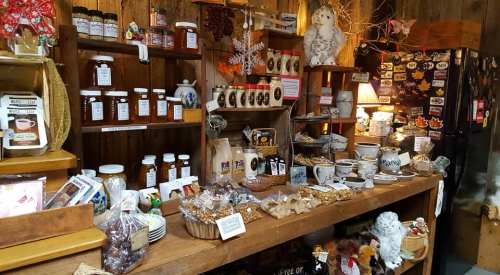 A cozy shop display featuring jars of honey, baked goods, and various local products on wooden shelves.
