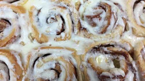 Close-up of freshly baked cinnamon rolls topped with creamy icing, arranged in a circular pattern.