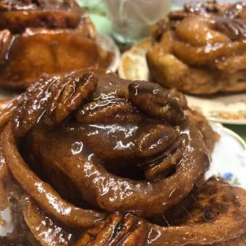 Close-up of sticky cinnamon rolls topped with pecans, glistening with syrup on decorative plates.
