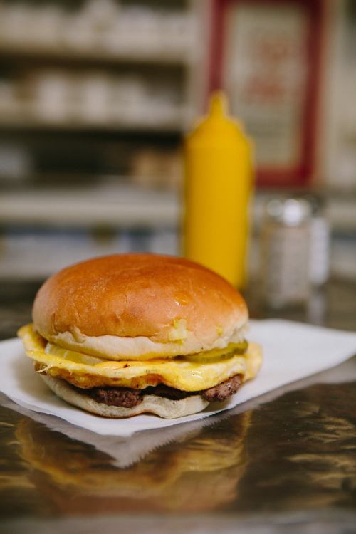 A close-up of a burger with a fluffy bun, cheese, and egg, served on a napkin with mustard in the background.