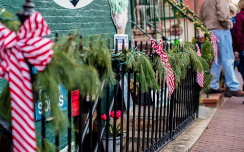 A festive fence adorned with green garlands and red-striped ribbons, with people in the background.