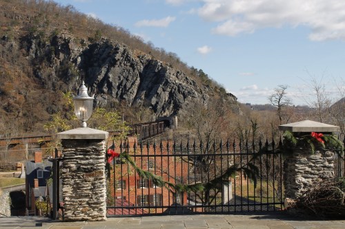 A scenic view of a rocky hillside with a decorative gate adorned with greenery and a lantern in the foreground.