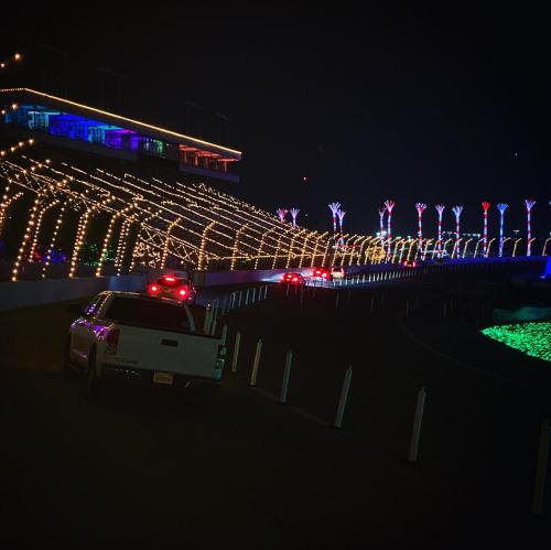 A nighttime scene of a racetrack adorned with colorful lights, with cars driving along the illuminated path.