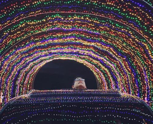 A person gazes up at a colorful tunnel of lights, creating a vibrant and festive atmosphere.